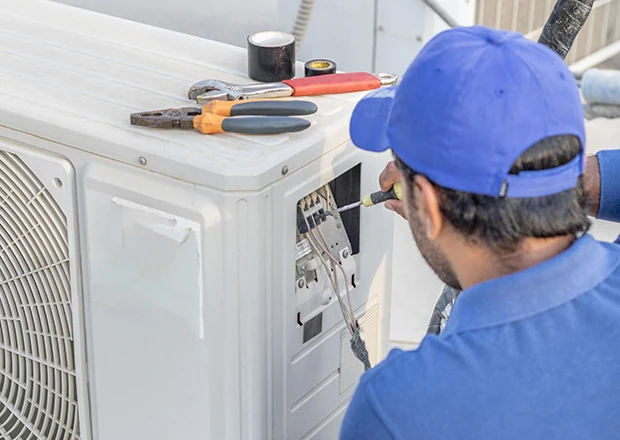 Technician repairing an outdoor air conditioner with tools close at hand